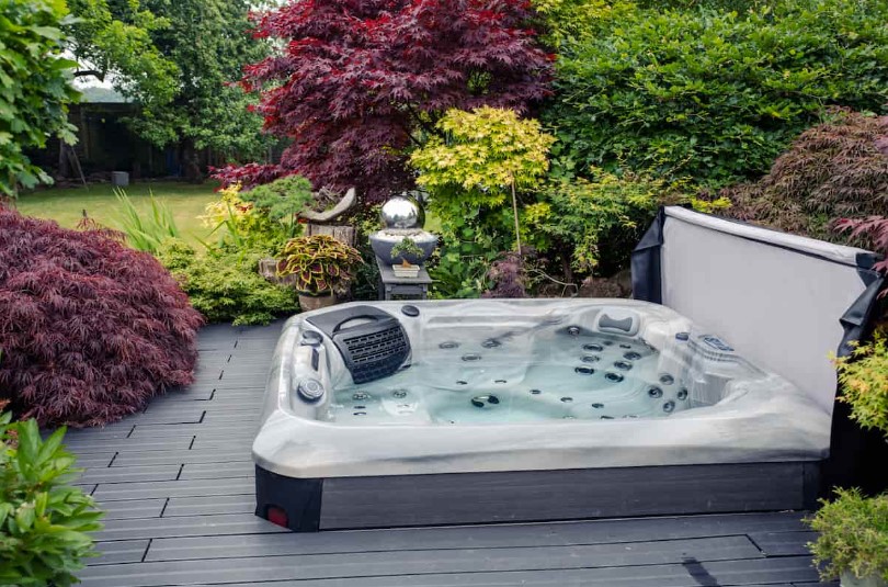 A Platinum Spas Santorini hot tub, installed on a deck, surrounded by foliage.